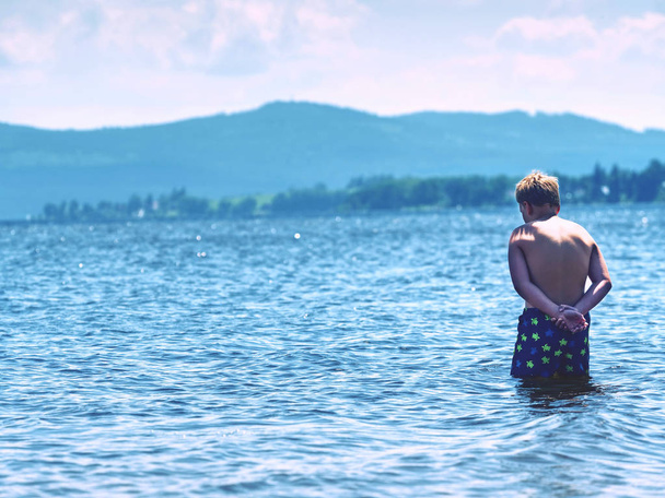 Młody chłopak w niebieskich szorty kąpielowe pobyt w zimnej wodzie jeziora - Zdjęcie, obraz