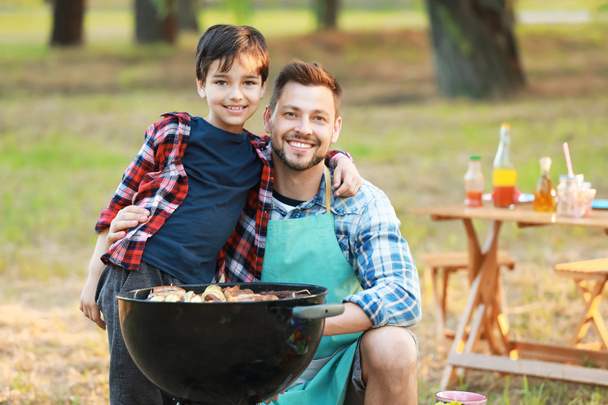 屋外のバーベキューグリルでおいしい食べ物を調理する父親と小さな男の子 - 写真・画像