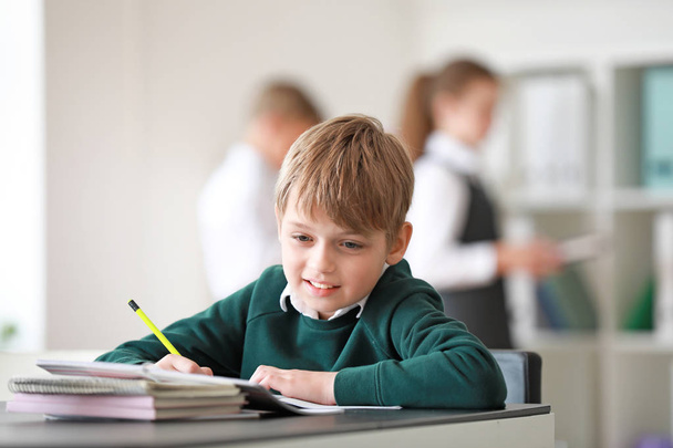 Cute little schoolboy doing lessons in classroom - Foto, Imagen