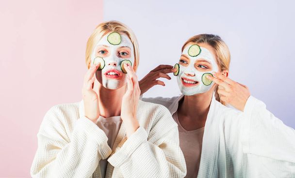 Conception of skin care by using fresh cucumber rings and white mask on the face. Two female sisters have weekend at bedroom. - Photo, image