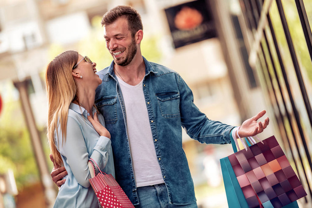 市内の店の窓の近くを歩くショッピングバッグを持つ幸せな若いカップル  - 写真・画像