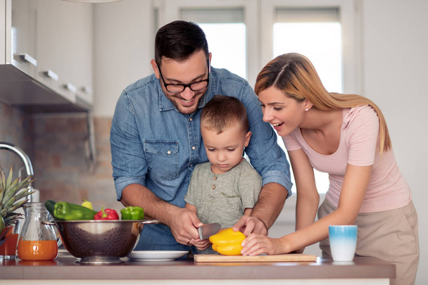 Glückliche junge Familie bereitet Mittagessen in der Küche zu und genießt gemeinsam.  - Foto, Bild
