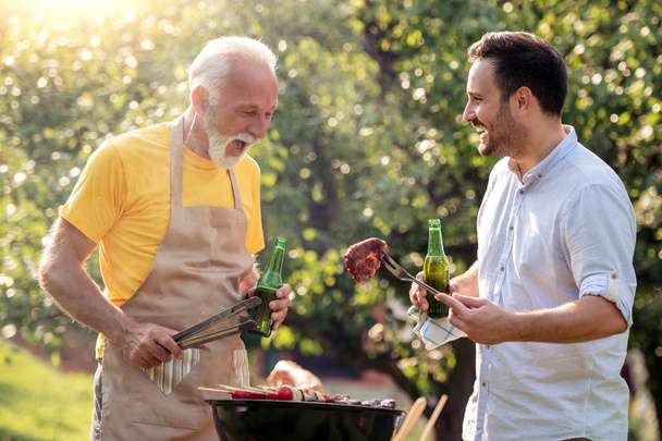 Тато і син зробити барбекю і пити пиво в саду. - Фото, зображення