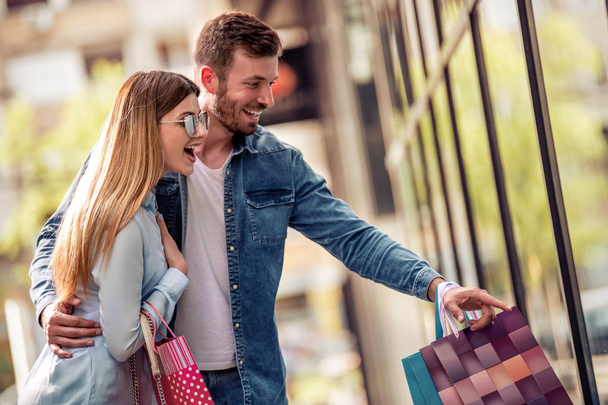 Jovem casal feliz com sacos de compras andando perto da janela da loja na cidade
  - Foto, Imagem