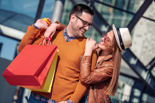 Kaunis nuori rakastava pari kuljettaa ostoskasseja ja nauttia yhdessä kävellessään kaupungissa aurinkoisena päivänä
  - Valokuva, kuva