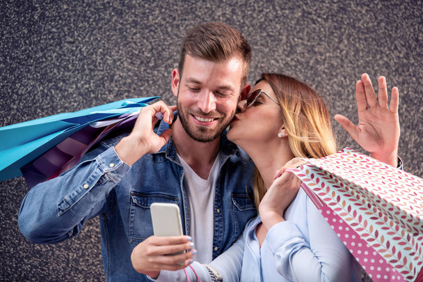 Glückliches Paar mit Einkaufstüten macht Selfie mit Smartphone - Foto, Bild