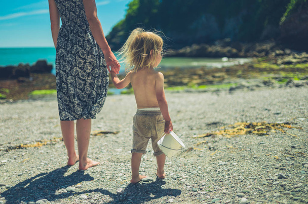 Genç bir anne güneşli bir yaz gününde sahilde onu bebek ile el ele yürüyor - Fotoğraf, Görsel
