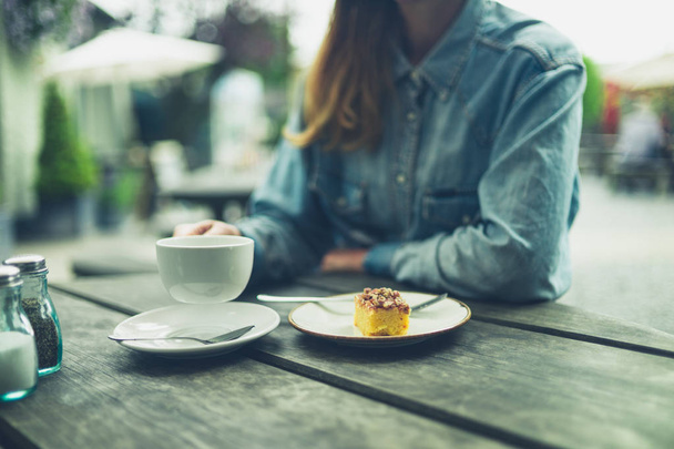 A young woman is drinking coffee and eating cake in nature - Foto, Imagen
