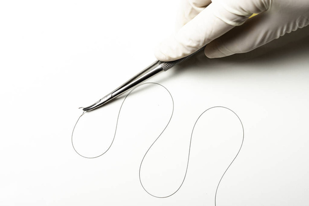 Doctor sosteniendo el soporte de la aguja sobre fondo blanco. Hilo de sutura. Hilo quirúrgico de nylon
. - Foto, imagen