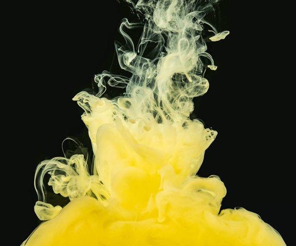 Yellow-white acrylic cloud dissolving into water, isolated on black background, close up view. Ink mixing with liquid. Abstract black background. Ready to use blending mode to screen or add. - Foto, afbeelding