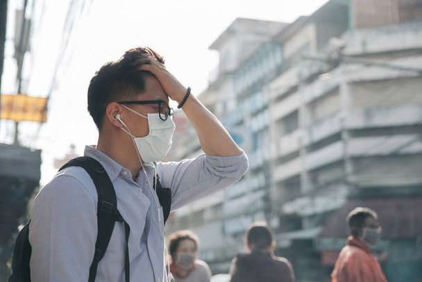 Asian man wearing a mask and holding his head on the street. Pro - Photo, image
