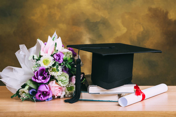 Graduation cap, hat with degree paper and flower bouquet on wood - Photo, image