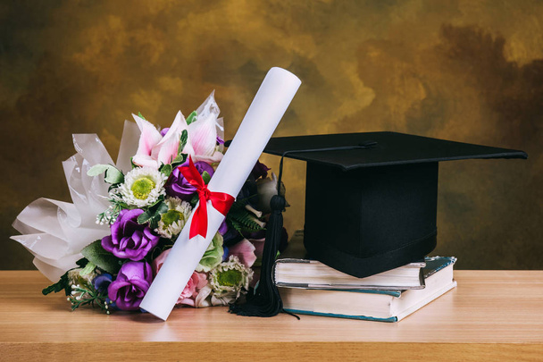 Graduation cap, hat with degree paper and flower bouquet on wood - Foto, Bild