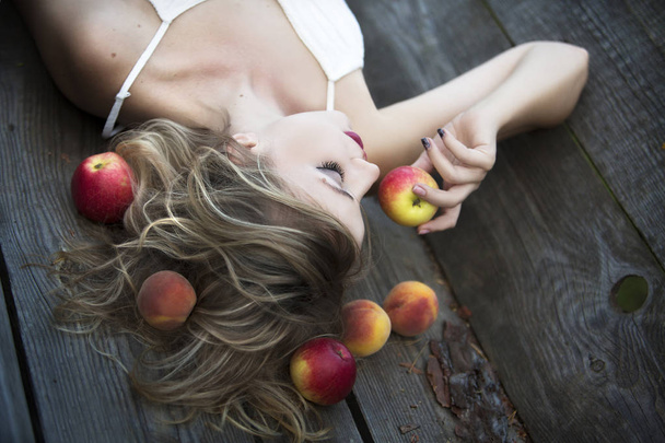 木製の背景に横たわって熟したリンゴを食べる美しい若い女性 - 写真・画像