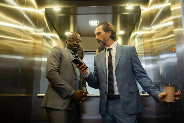 Grey-haired man talking to business partner while using elevator - Foto, Imagem