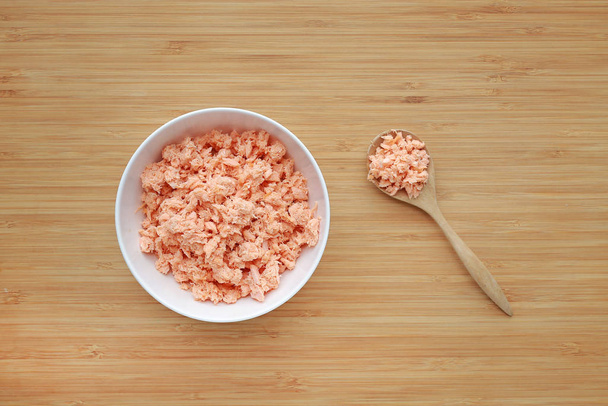 Shredded salmon fish in white bowl on wooden board background. - Photo, image