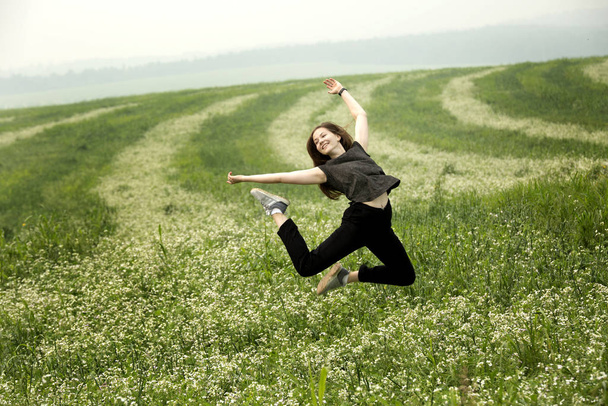 A young girl is jumping in a field. Dressed in black clothes - Fotografie, Obrázek