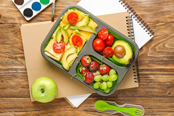 School Lunchbox met lekker eten en briefpapier op houten tafel - Foto, afbeelding