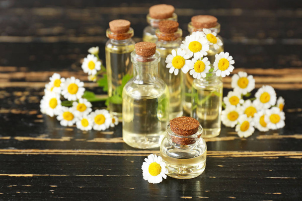 Пляшки ефірної олії з квітами ромашки на темному столі
 - Фото, зображення