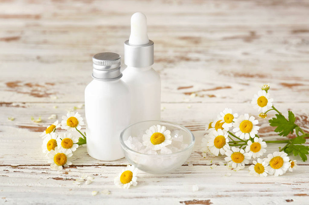Bottles of cosmetic product with chamomile flowers on white table - Photo, Image