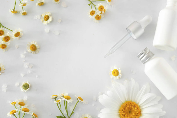 Frame gemaakt van cosmetische producten met kamille bloemen op witte achtergrond - Foto, afbeelding