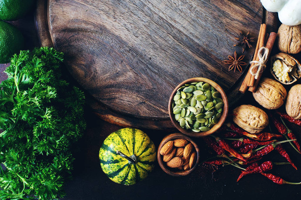 Autumn background with decorative pumpkin, seeds, nuts, greens, fruits, vegetables, spices  and wooden board with space for text  - Foto, afbeelding