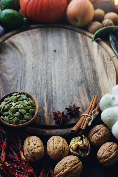 Autumn background with decorative pumpkin, seeds, nuts, greens, fruits, vegetables, spices  and wooden board with space for text  - 写真・画像