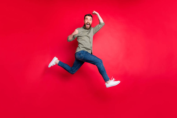 Full length body photo of bearded strong sporty handsome white man wearing grey t-shirt running somewhere with victory while isolated with red background - Foto, Bild