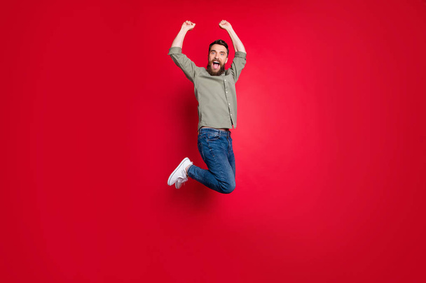Full length body size photo of rejoicing happy man jumping with victory while isolated with red background - Фото, зображення