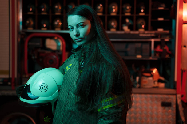 Image of woman firefighter with long hair with helmet in her hands at fire station. - Valokuva, kuva