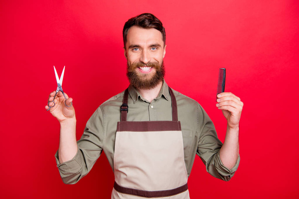 Close-up portrait of his he nice attractive cheerful cheery bearded guy salon owner holding in hands instruments choose choice isolated over bright vivid shine red background - Φωτογραφία, εικόνα
