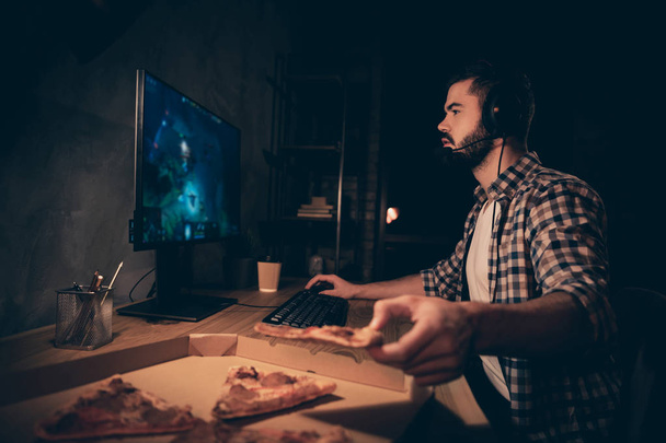 Close up side profile view photo he him his guy videogame talk headset microphone strategy teammates concentrated look screen eat pizza wear casual plaid checkered shirt internet cafe table indoors - 写真・画像
