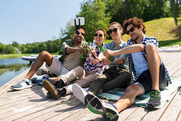 friends with drinks taking selfie on lake pier - Foto, afbeelding