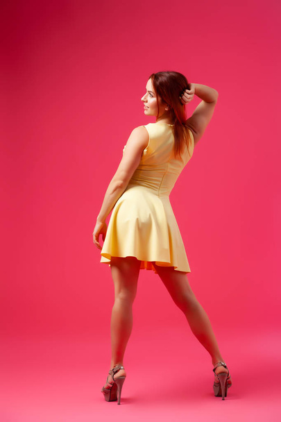 Giovane donna seducente in un abito giallo nello stile di un nuovo look turbinii, pose e si diverte su uno sfondo rosa isolato. Il concetto di bellezza e grazia femminile, in posa in uno studio fotografico
 - Foto, immagini