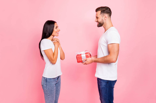 Photo of man wearing t-shirt presenting his gift to his amazed astonished girlfriend looking into her excited eyes while isolated with pink background - Photo, Image