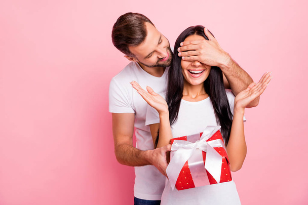 Photo of cute nice couple of fallen in love liking to gift each other red package with bow while isolated with pink background - Фото, изображение