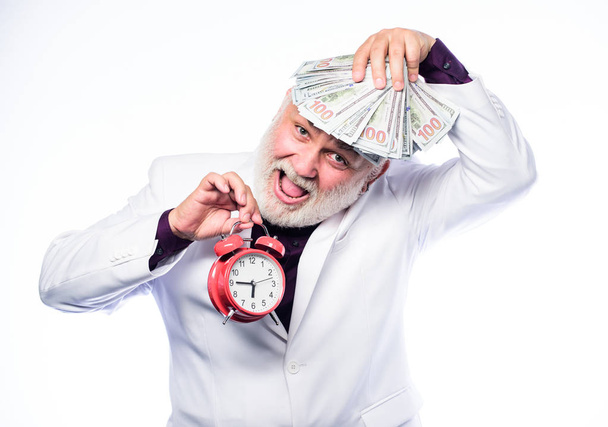 Pieniądze. Dojrzały mężczyzna z brodą trzyma pieniądze. Czas na pokaz zegarów. Czas to pieniądz. zarządzanie czasem. sukces biznesowy. emeryturę. czas i wiek. Pilnowanie czasu. dojrzały brodaty mężczyzna z budzikiem - Zdjęcie, obraz