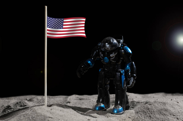 Robotic astroneer in black space suit put a american flag into the surface of the planet in outer space at the rim light of star - Zdjęcie, obraz