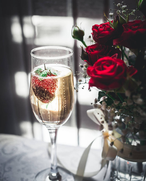 Glass of champagne with strawberry and red roses - Foto, afbeelding