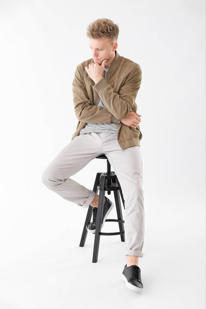 Stylish young man sitting on stool against white background - Photo, Image