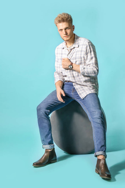 Стильний молодий чоловік сидить на пуфі на кольоровому фоні
 - Фото, зображення