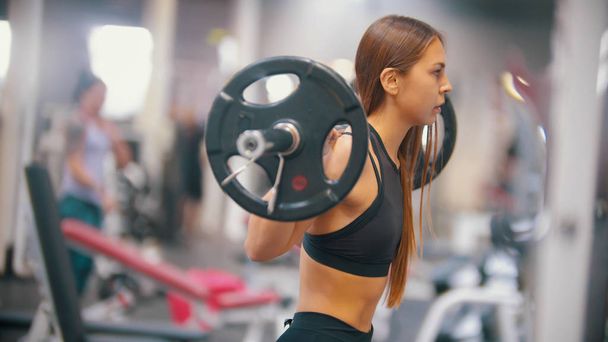 An athlete woman training in the gym - gets under the dumbbell and put it on her shoulders - Photo, image