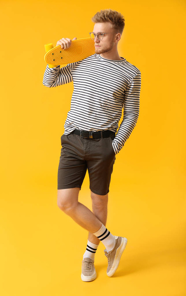 Stylish young man with skateboard on color background - Photo, Image