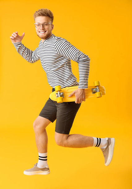 Stylish running young man with skateboard on color background - Photo, Image
