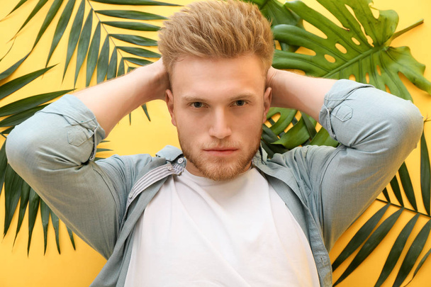 Stylish young man and tropical leaves on color background - Foto, afbeelding