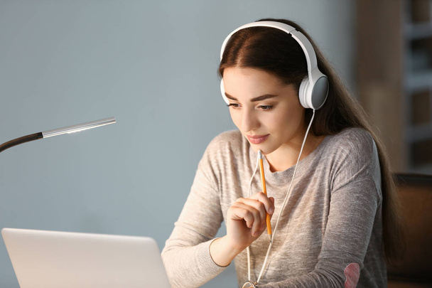 Γυναίκα φοιτητής με φορητό υπολογιστή ακούγοντας μουσική κατά την προετοιμασία για εξετάσεις στο σπίτι - Φωτογραφία, εικόνα
