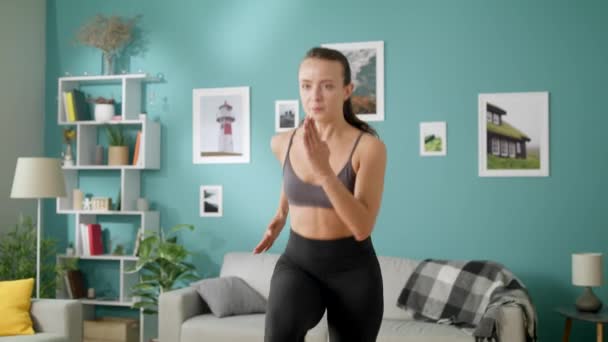 Beautiful woman does morning cardio exercises running on the spot in room - Filmati, video