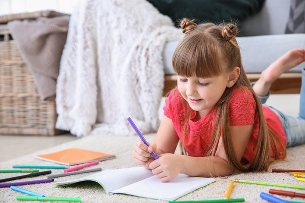 Schattig klein meisje tekenen terwijl liggend op tapijt - Foto, afbeelding