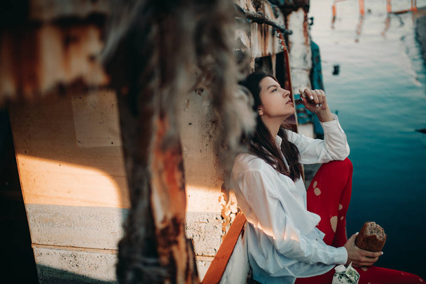 Una giovane donna siede e mangia pane su una vecchia nave abbandonata
. - Foto, immagini