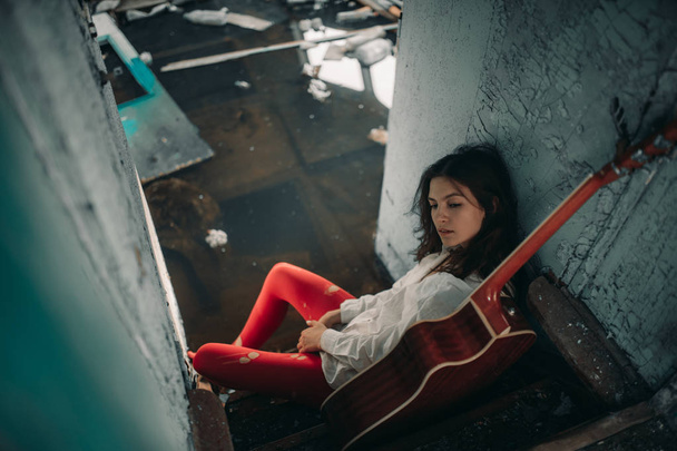 A young woman sits with guitar inside of old abandoned ship. - Photo, Image
